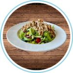 Greek salad with chicken on a white dish and wood background